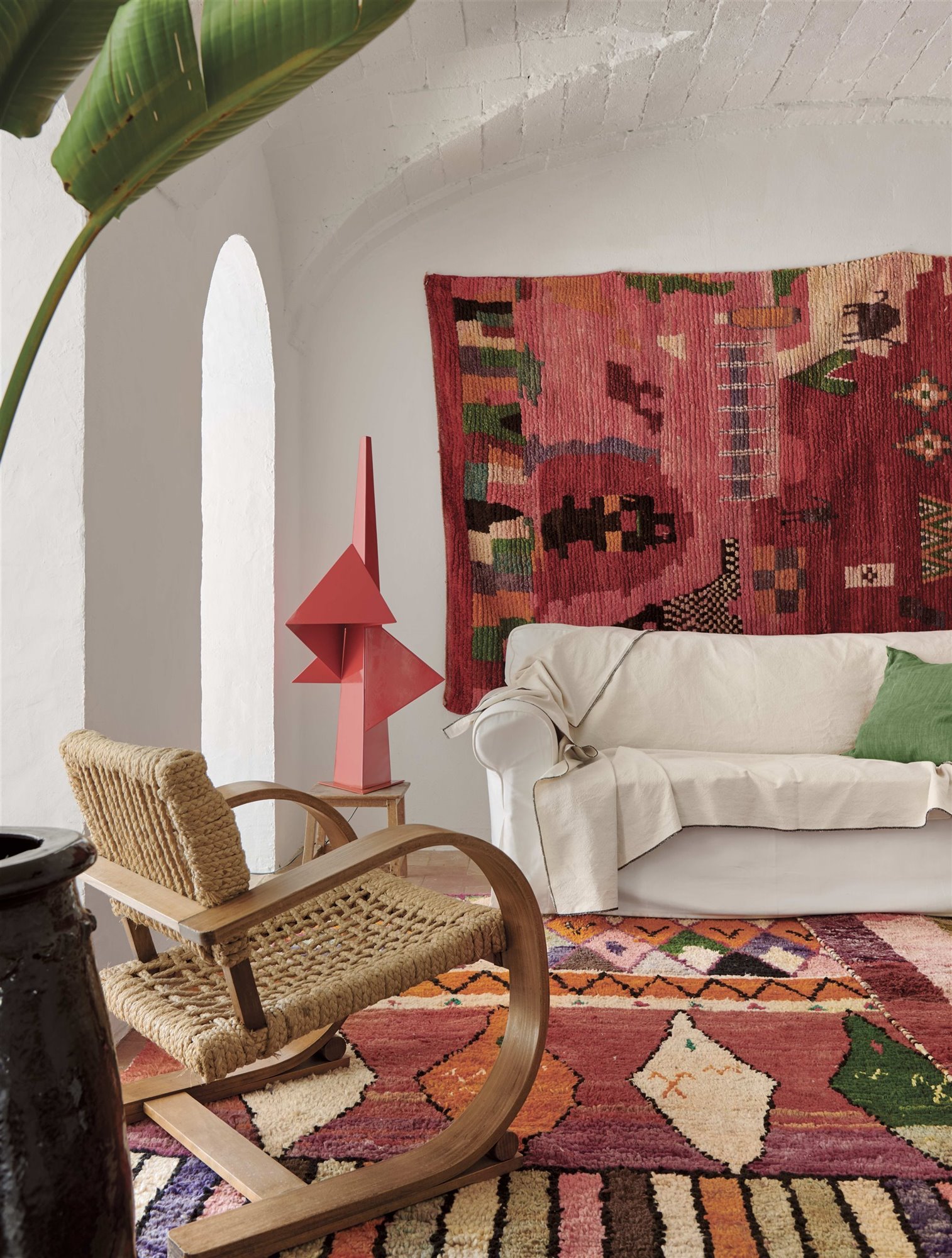 salón ecléctico alfombra marroquí, butaca de mimbre, sofá blanco, tapiz colorido y lámpara roja