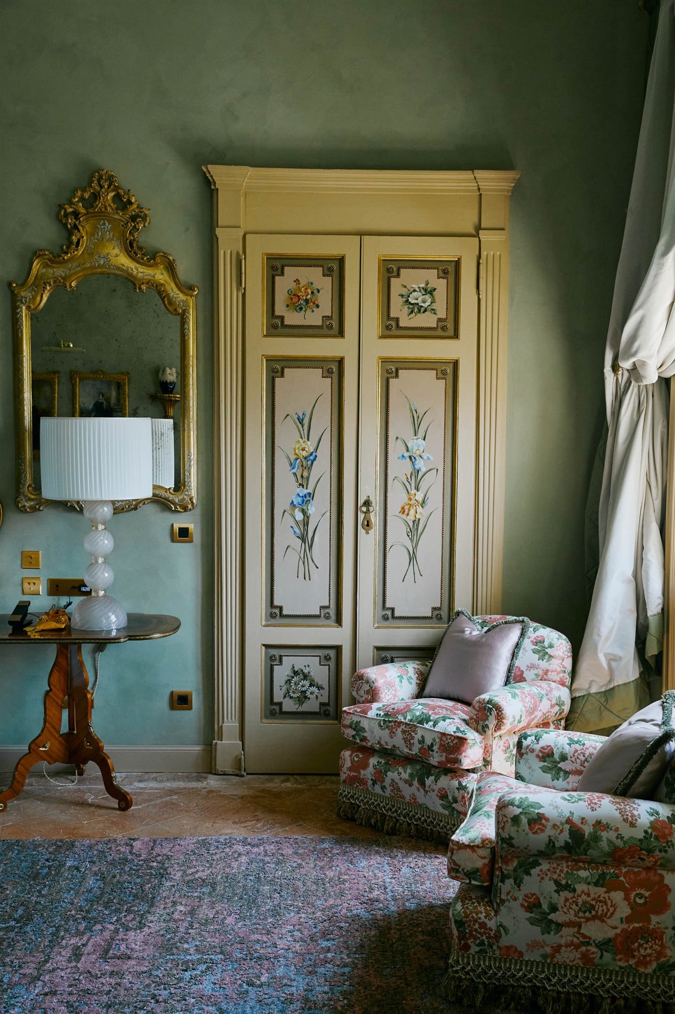 dormitorio con pared verde, butaca de flores, armario pintado y espejo dorado