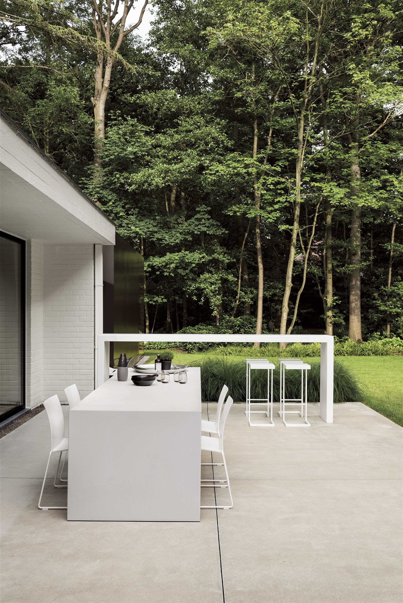 jardín con terraza de hormigón, mesa de comer blanca y barra de bar con taburetes