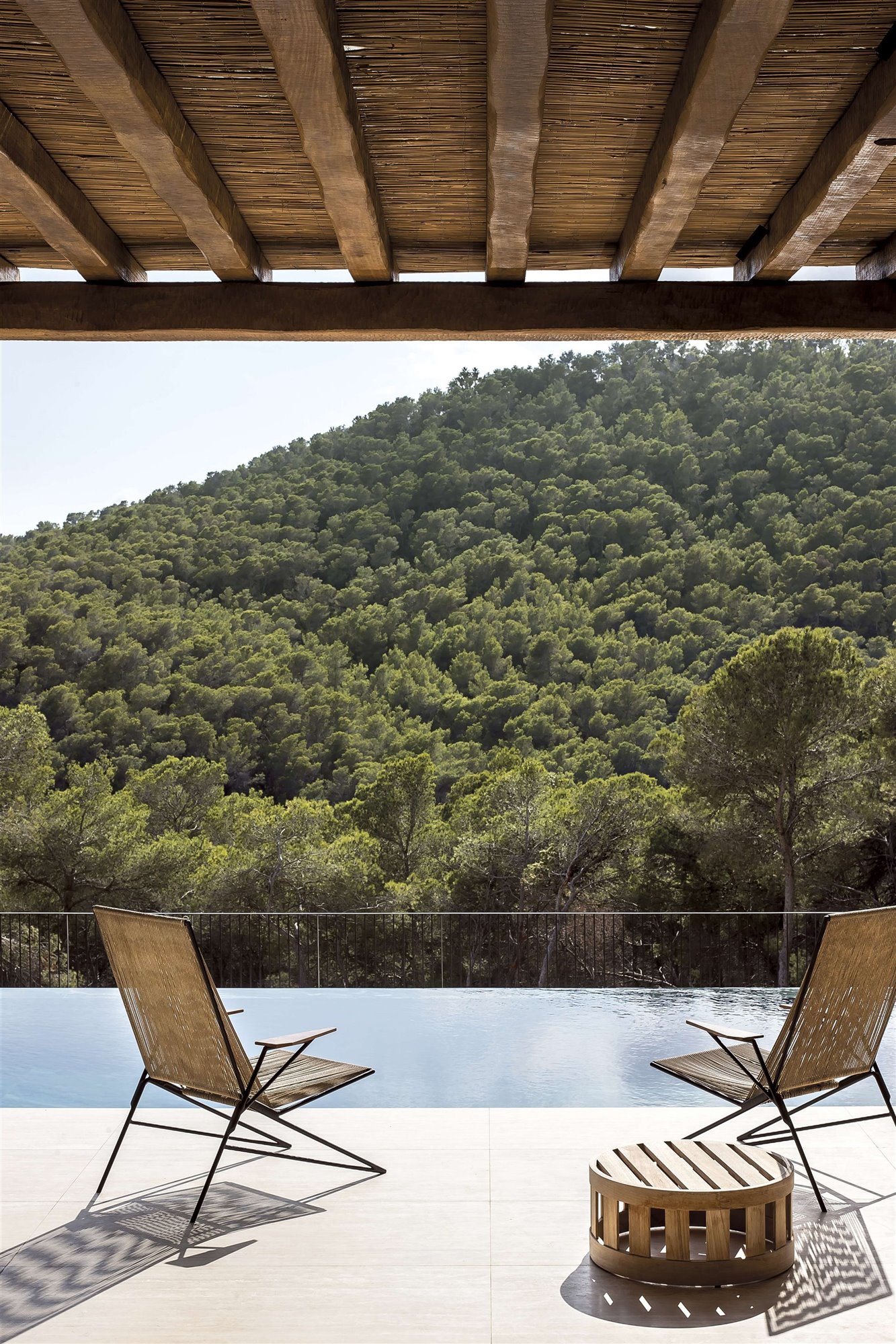 porche de casa mediterránea con techo de madera y piscina infinity, hamacas de fibra natural 