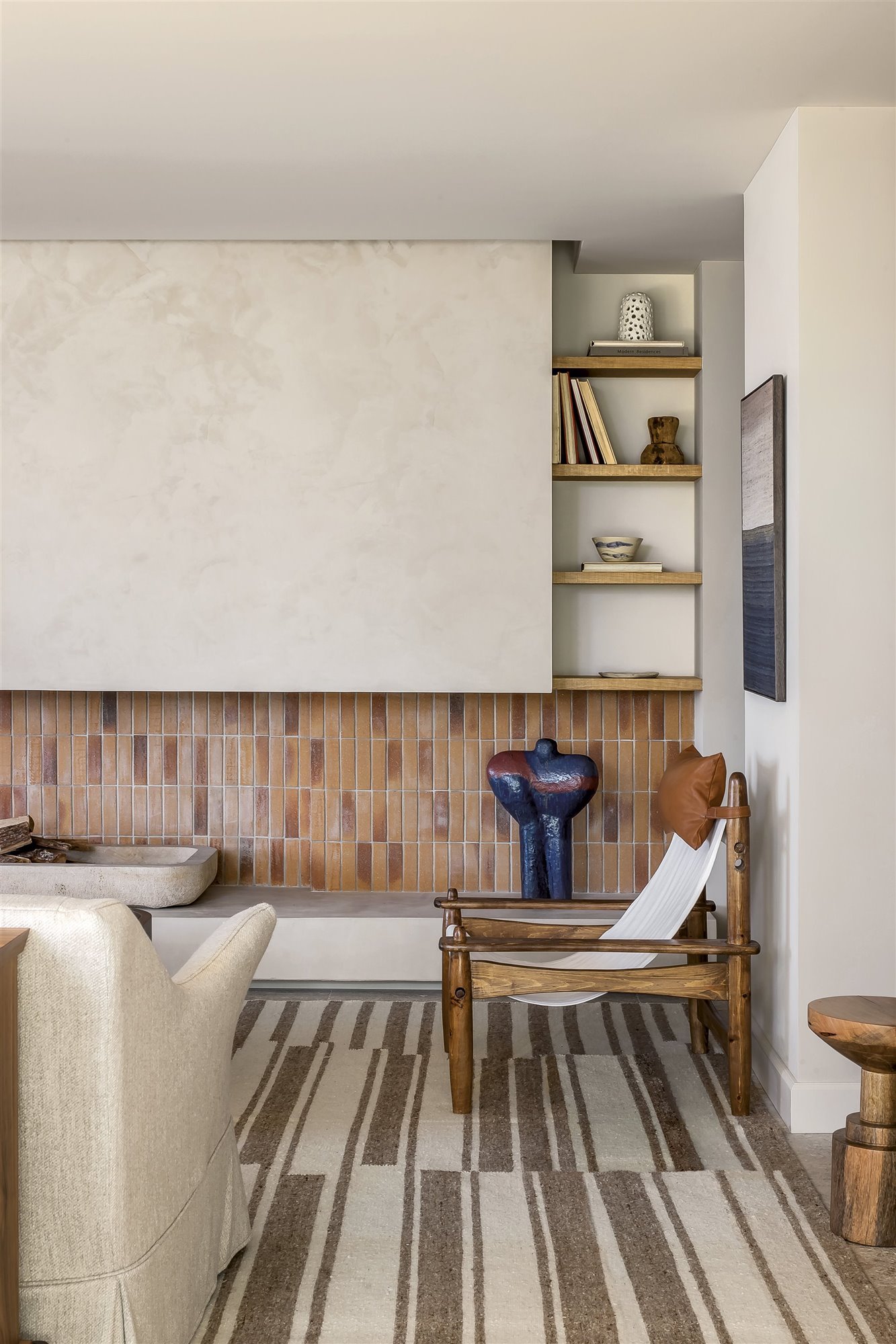 sala de estar con chimenea de ladrillo, silla de madera, sofá beige y estantería con libros