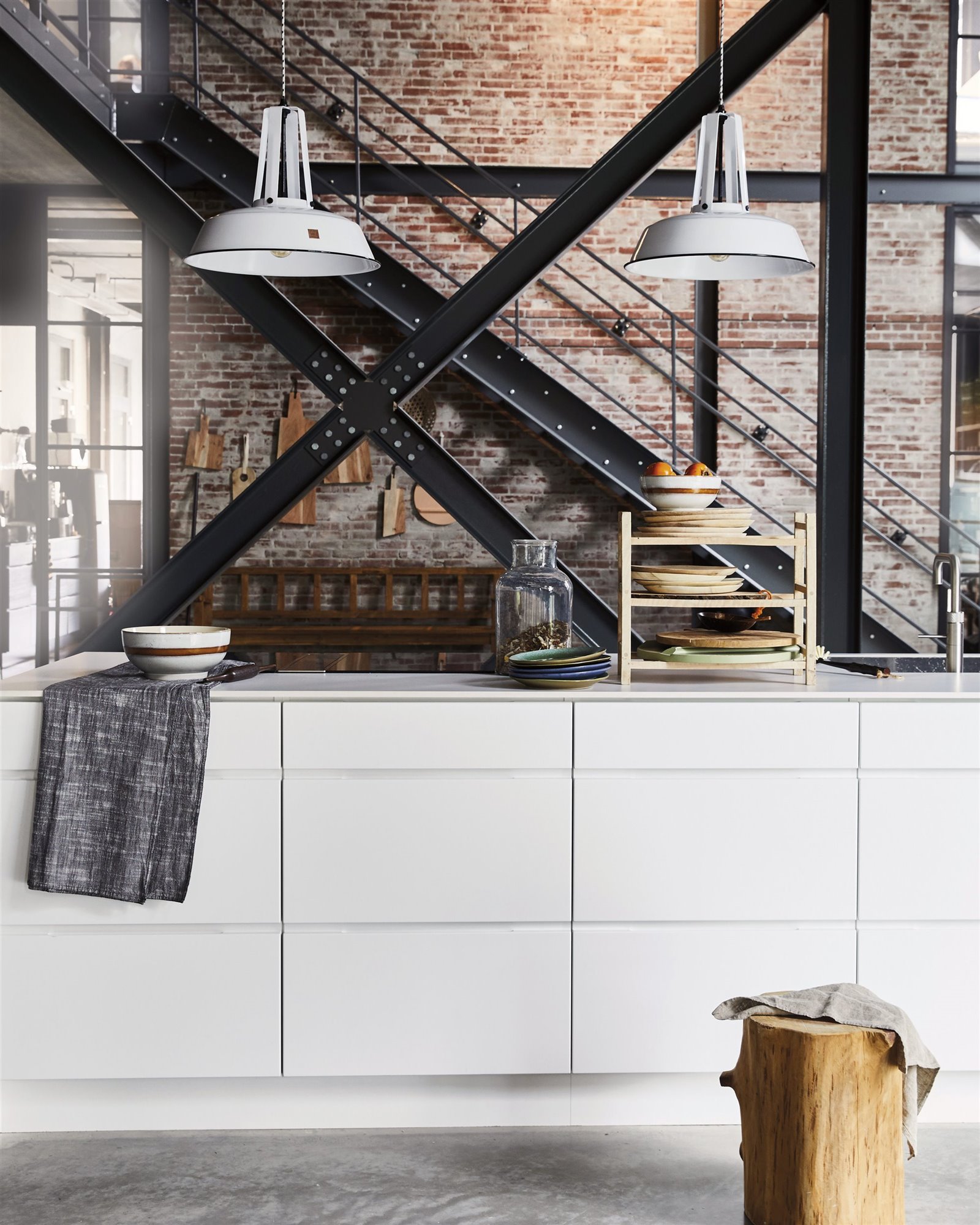 cocina industrial pared de ladrillo y vigas de metal negro con encimera blanca y lámparas de techo