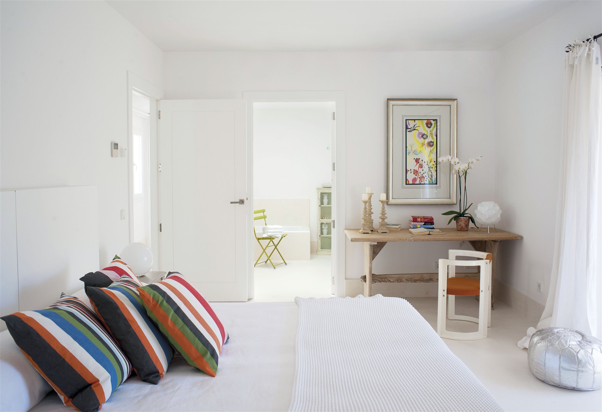 dormitorio blanco estilo boho con cojines estampados de colores, mesa de madera y silla naranja