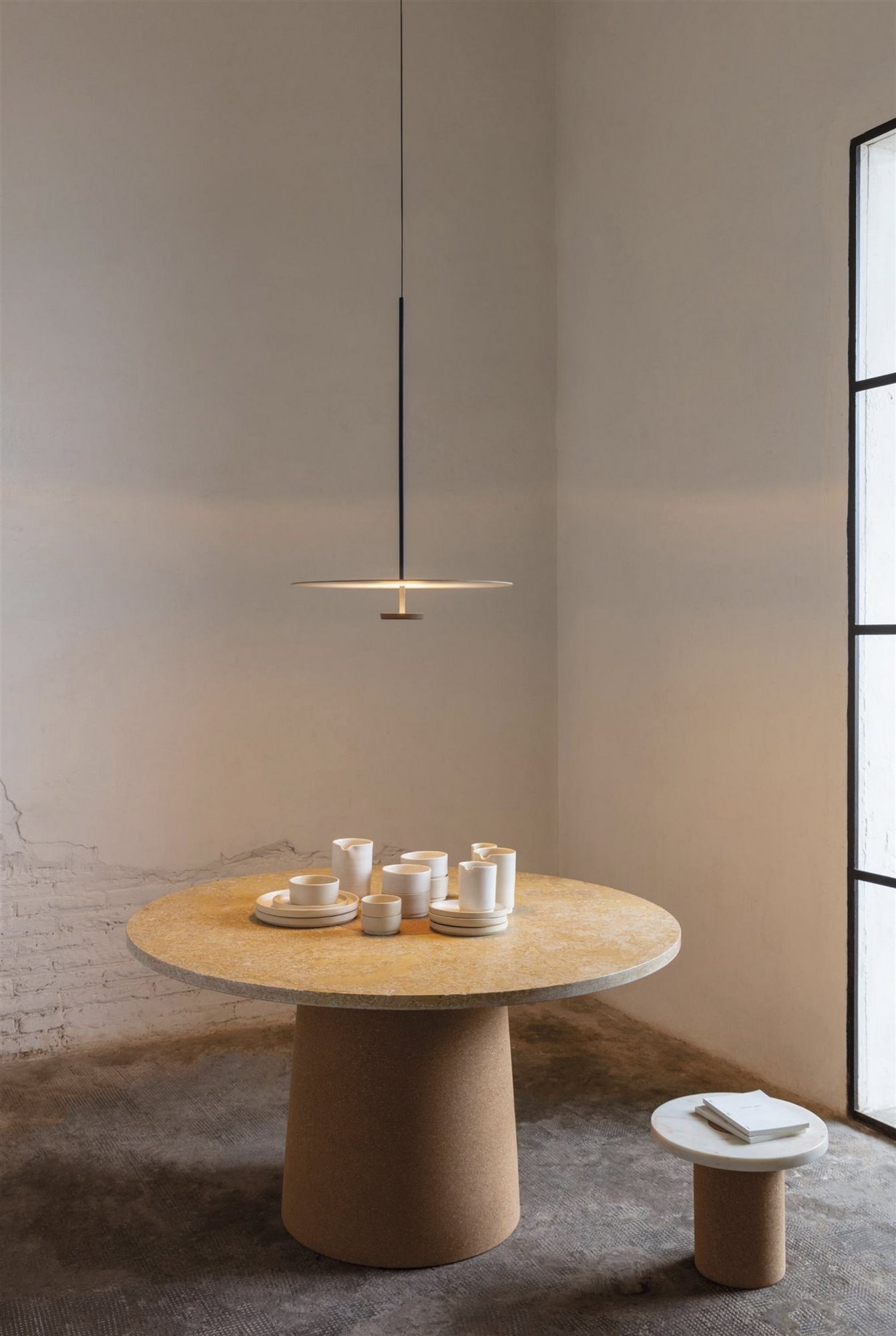 lámpara de techo negra minimalista y mesa de comedor redonda de madera con vajilla blanca y taburete