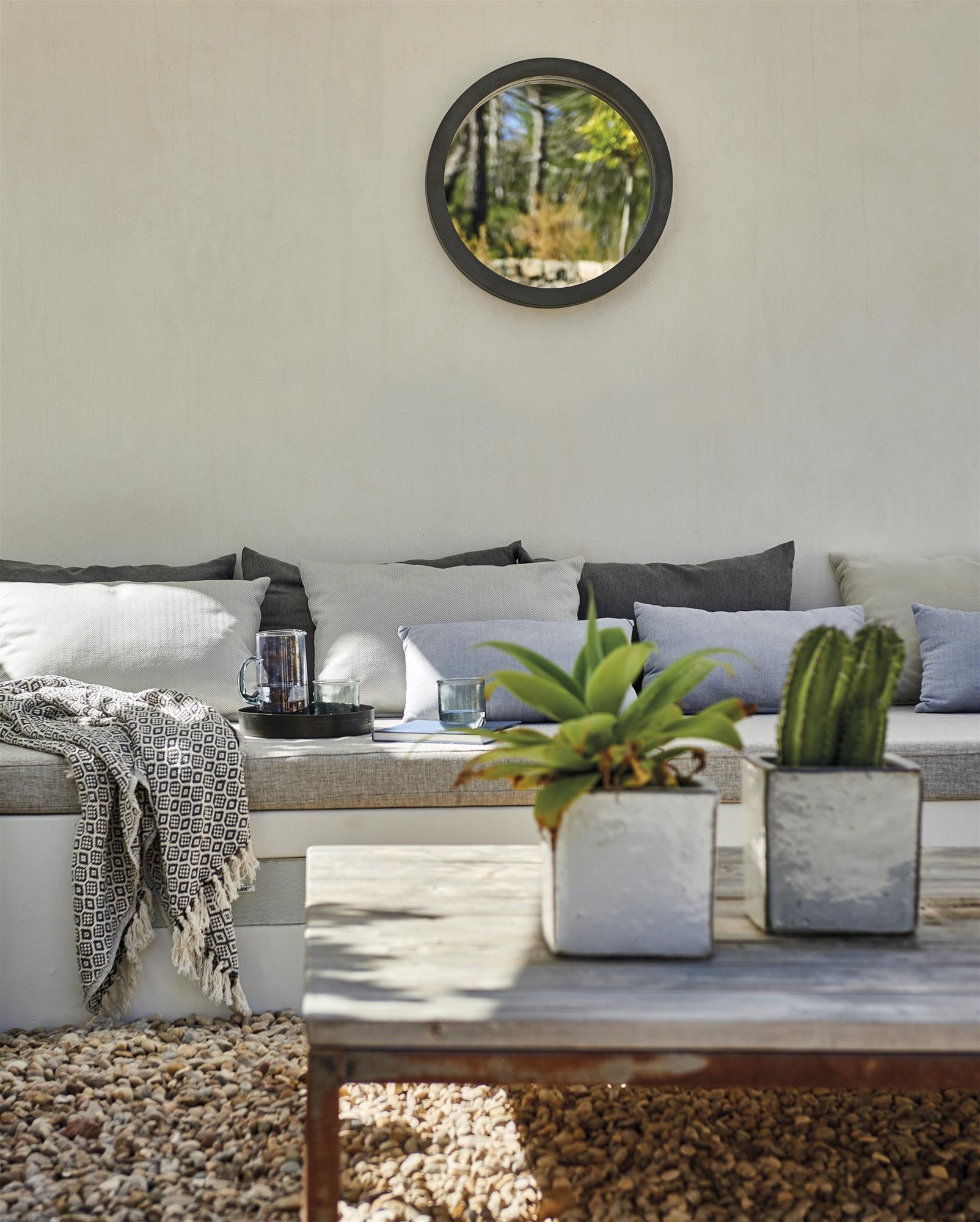 terraza con suelo de piedras y muebles de exterior banco con cojines y mesa de madera