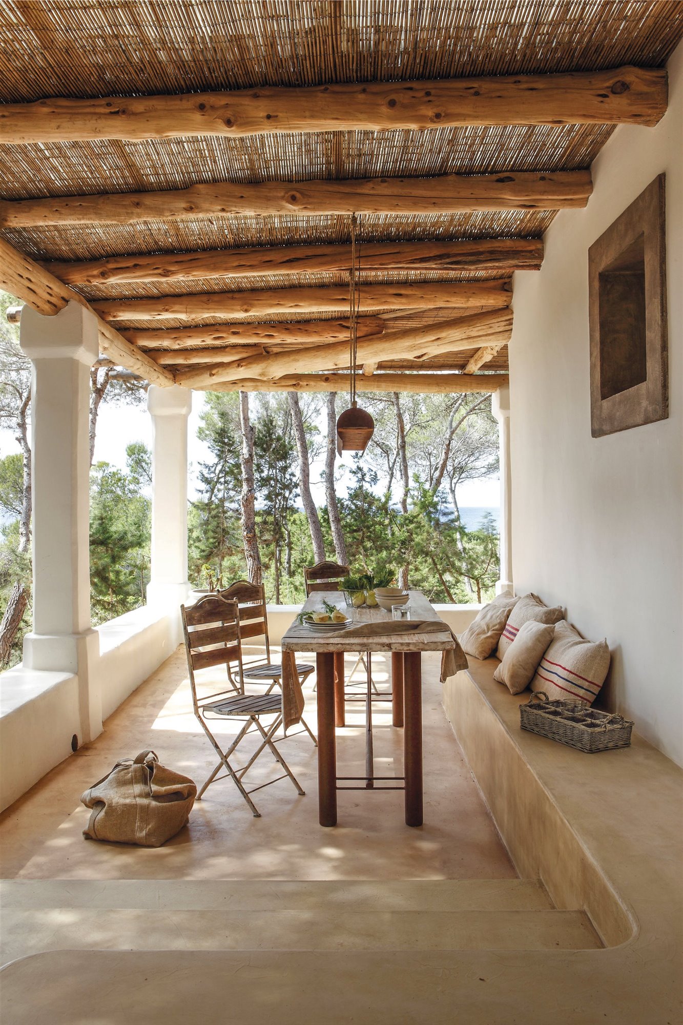 comedor en un porche rústico con techo de madera  y caño, banco de piedra y mesa y sillas