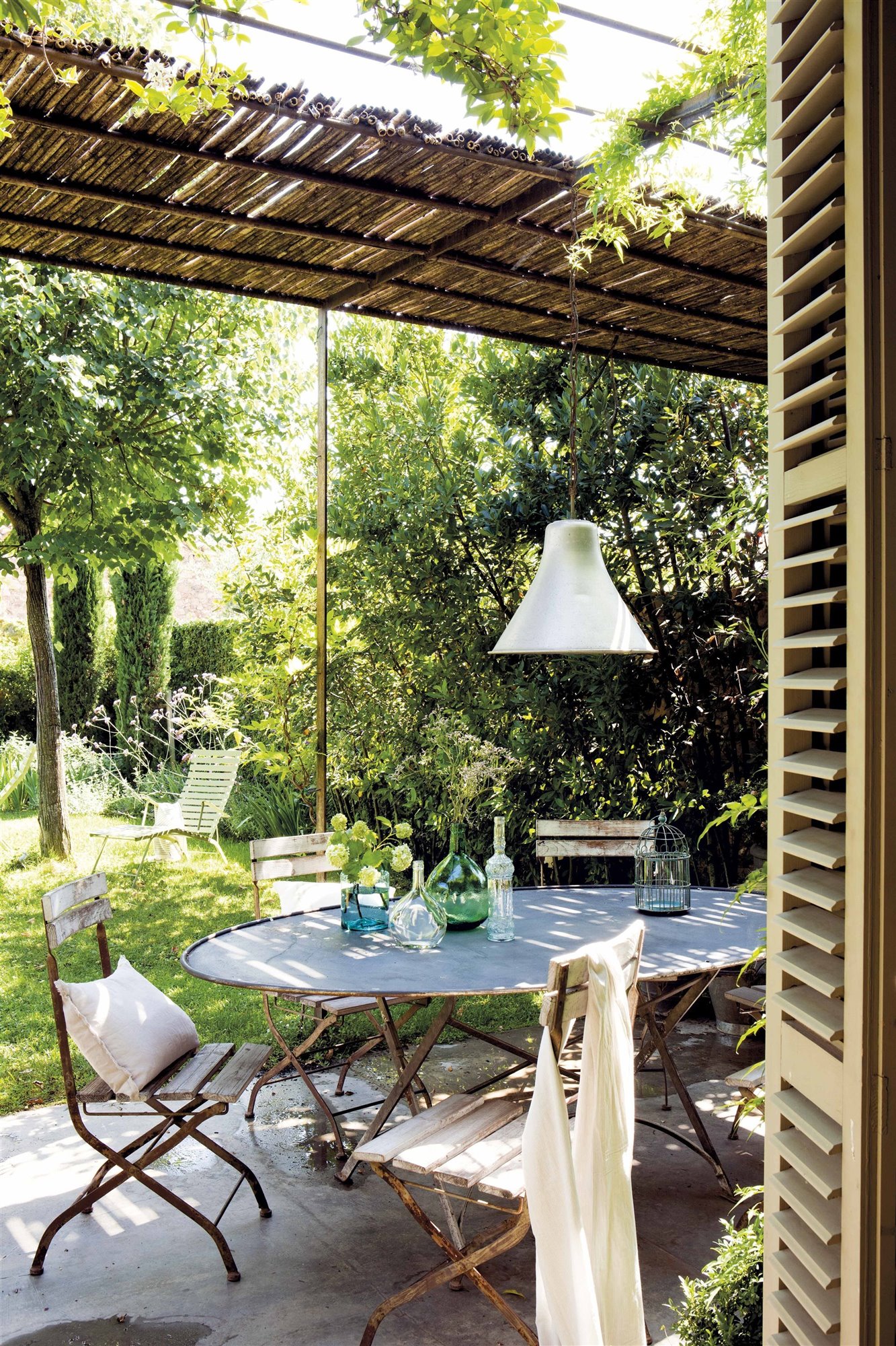 jardín con cenador mesa ovalada de metal y sillas rústicas