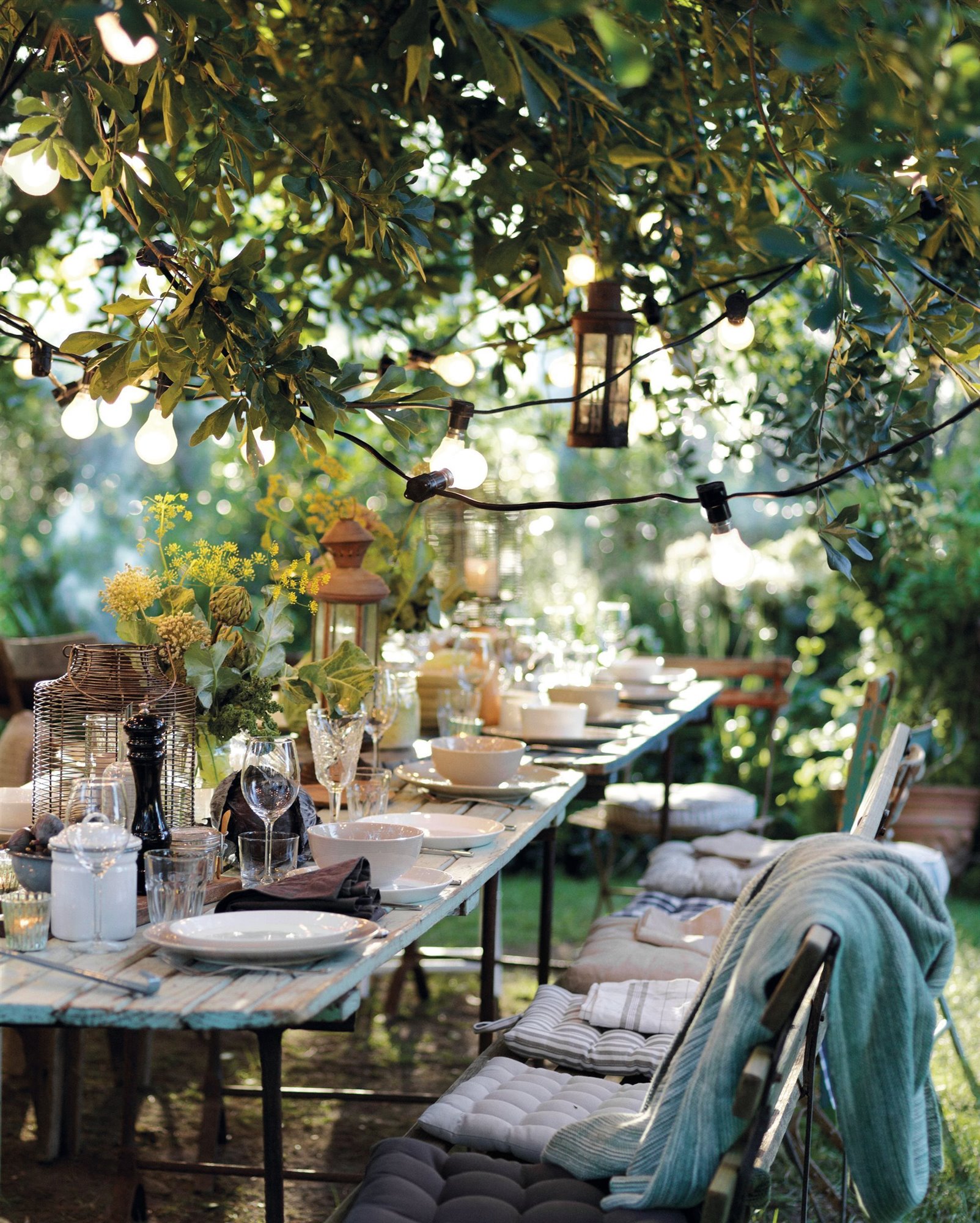 jardín romántico con mesa de comedor de madera y guirnalda de luces