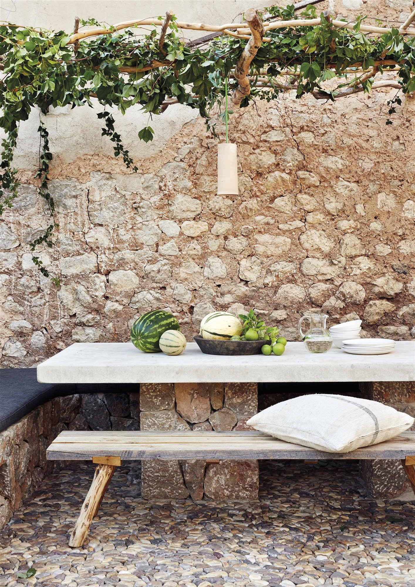 patio de piedra y hiedra con mesa de mármol con frutas y banco de madera