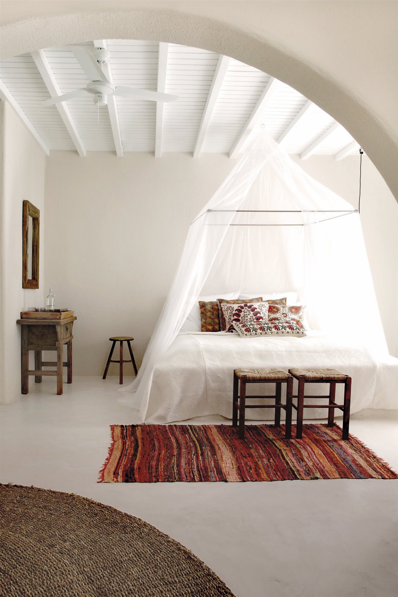 dormitorio boho con arco, mosquitera blanca, alfombra naranja y muebles de madera