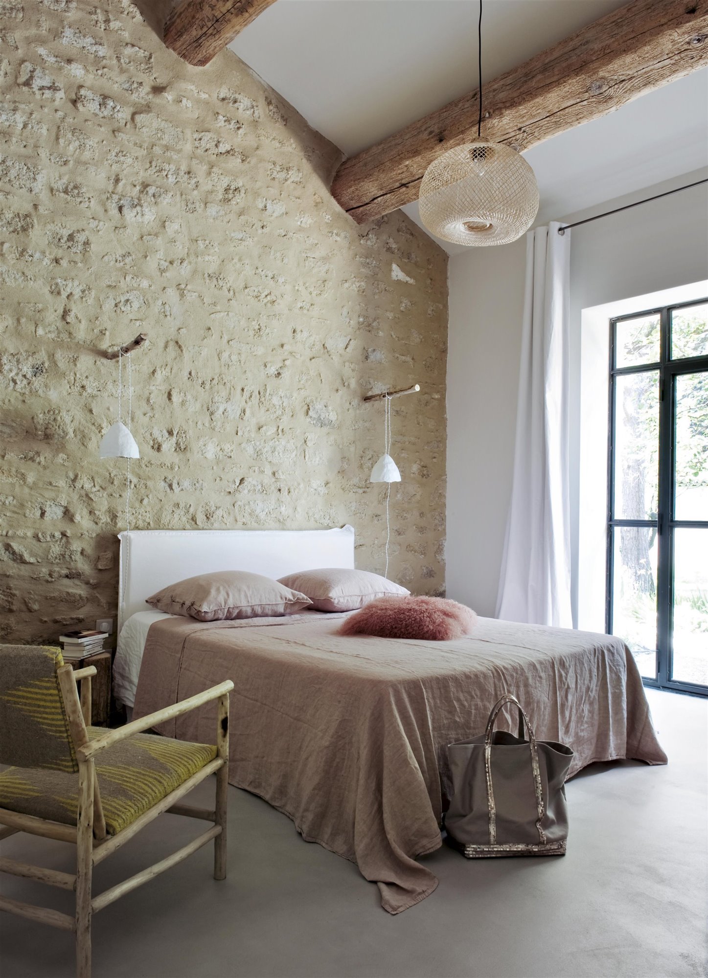 dormitorio rural pared de piedra y vigas de madera, cama rosa y butaca