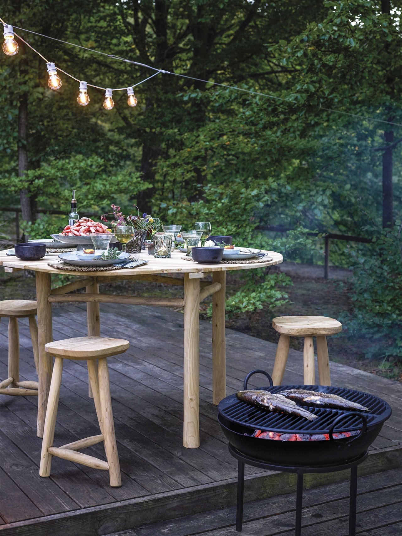 jardín con mesa de madera, barbacoa y guirnalda de luces