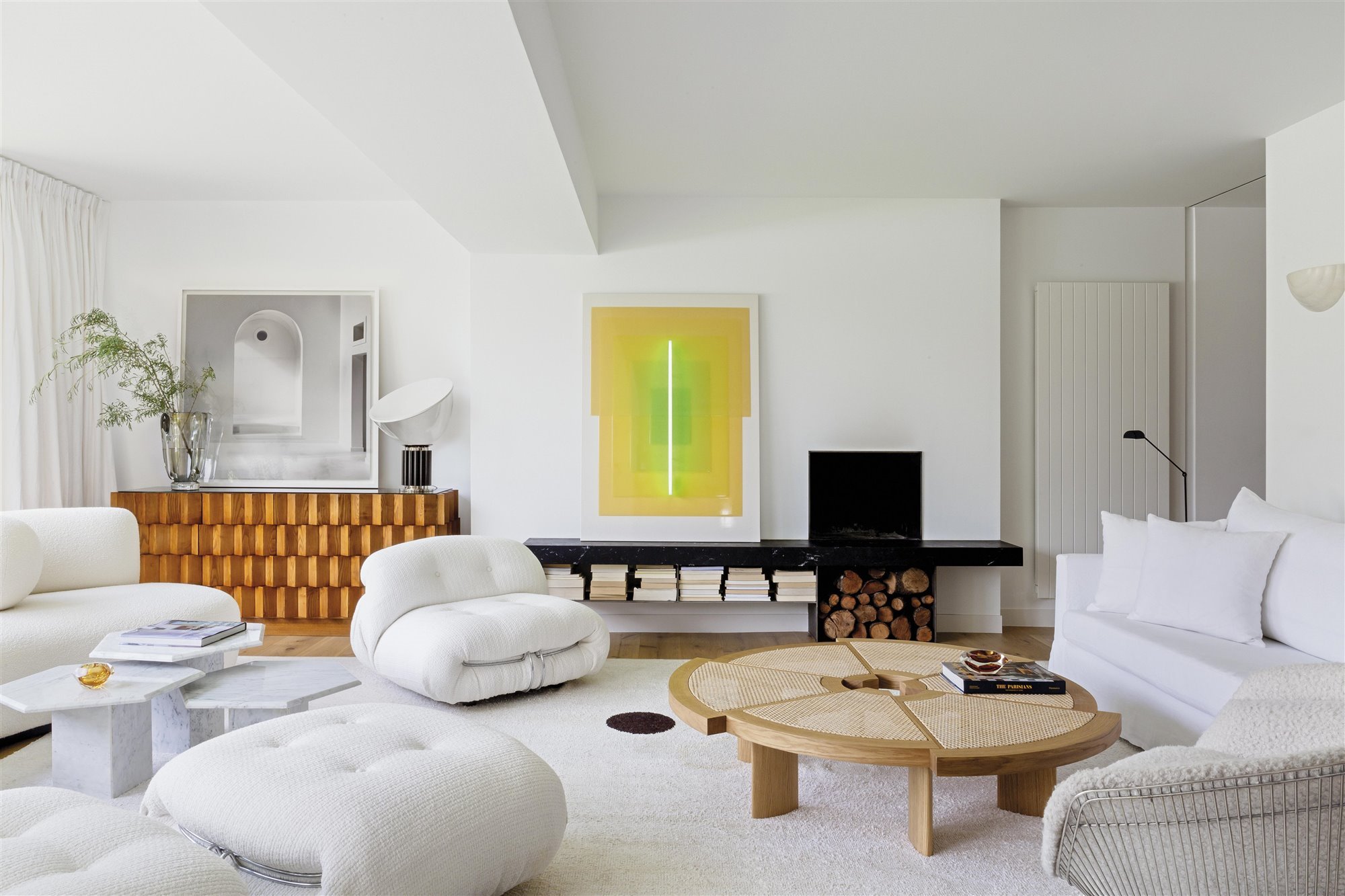 salón moderno y contemporáneocon sofás blancos, mesa de café redonda de madera, cuadros y chimenea
