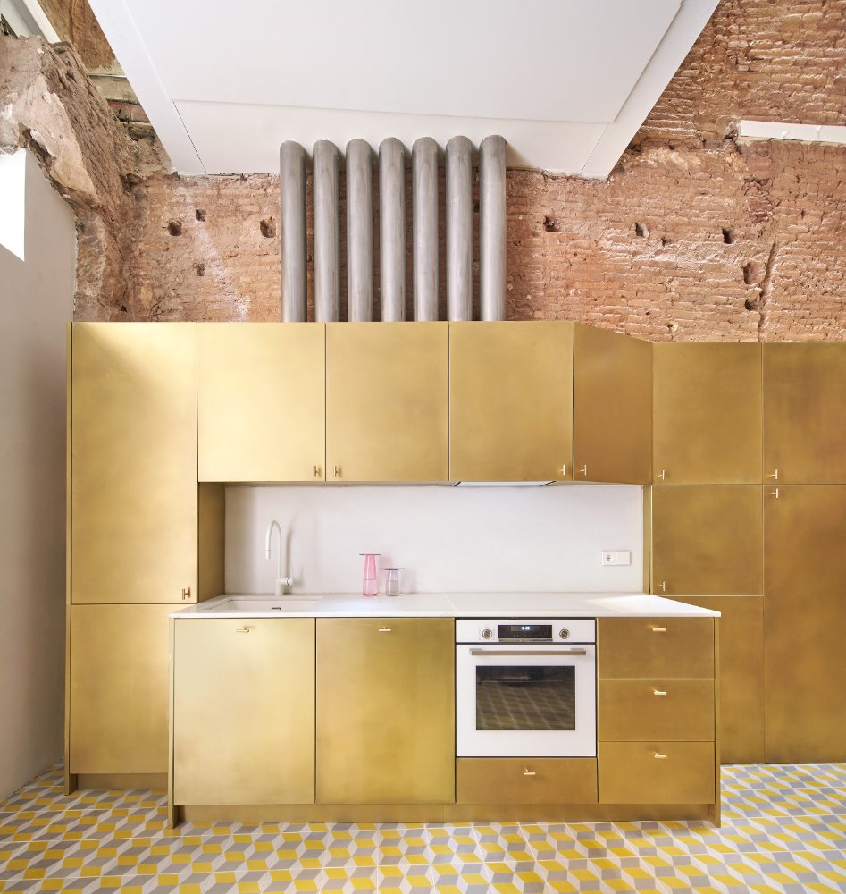 En la cocina de BSP20, Raúl Sánchez eligió puertas doradas para contrastar con el ladrillo. Encima de los armarios se ven los tubos de acero que conducen todas las instalaciones a todo el edificio en vertical. Uno de ellos se ha dejado vacío previendo futuras necesidades.