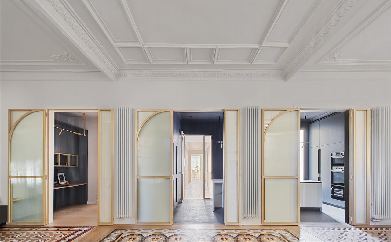 La cocina y el estudio se han ubicado en un espacio intermedio entre el salón y la zona más privada, comunicados por puertas de cristal con carpintería metálica de color bronce que evocan el estilo modernista.