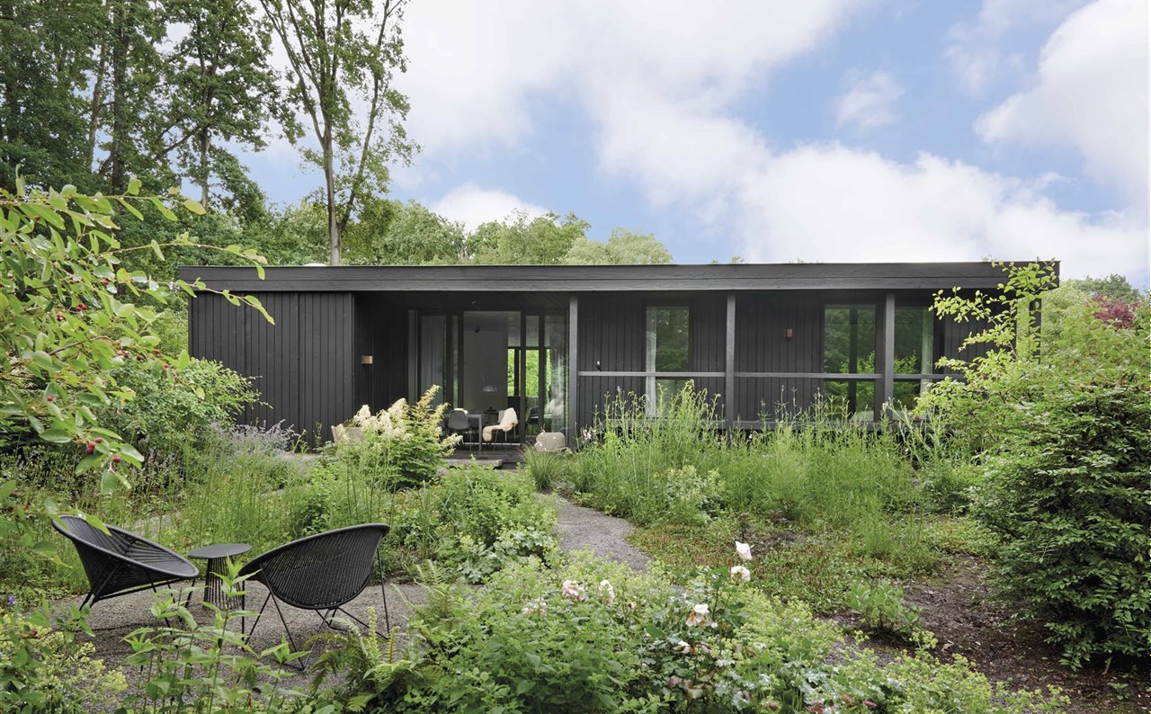 Esta casa revestida de madera quemada en un bosque de Bélgica busca la conexión entre los espacios interiores y los exteriores. En el jardín, junto al sendero, butacas C317, diseño de Yuzuru Yamakawa para Feelgood.