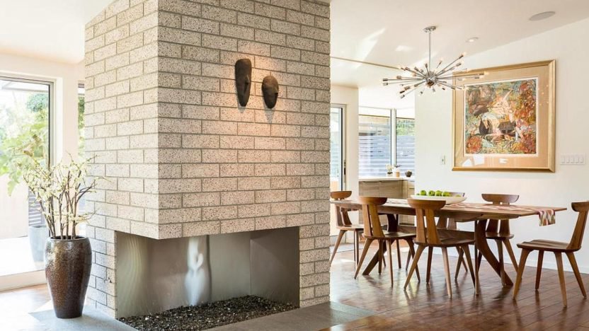 Comedor modernista con chimenea de piedra y mesa mid century de madera