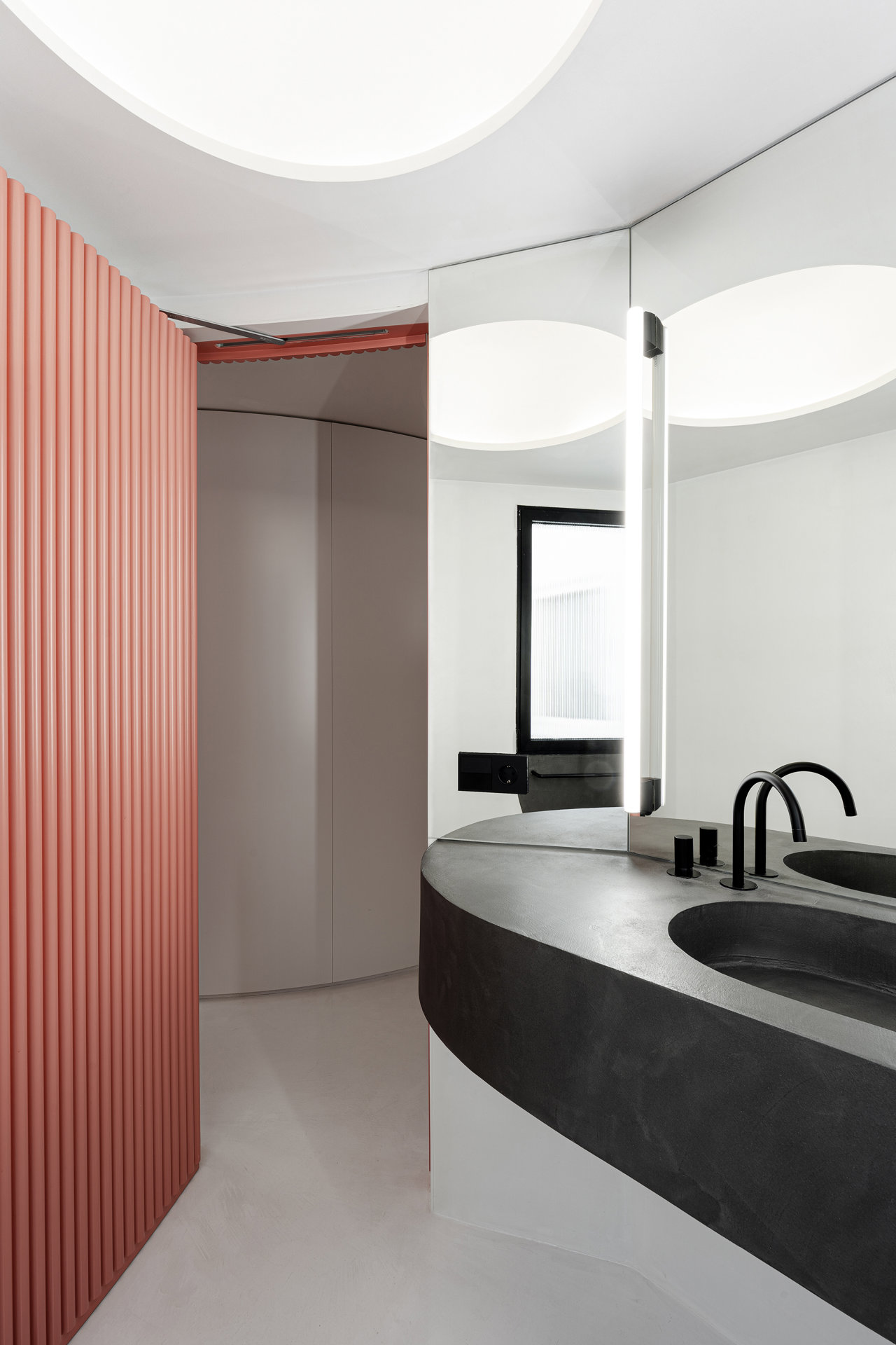 El baño se esconde dentro del volumen curvo revestido con un panelado en color salmón en el que la puerta queda escondida. 