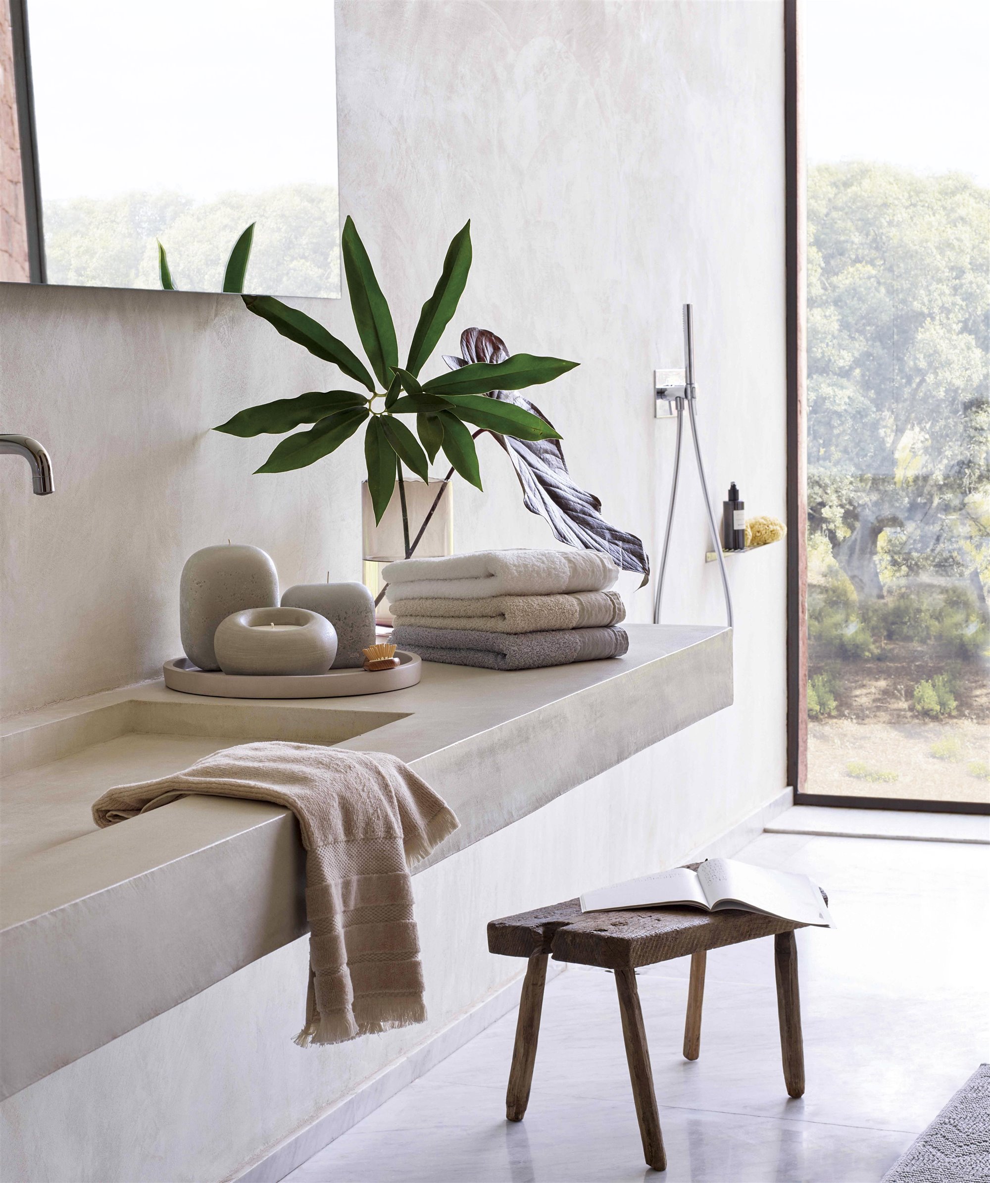 Baño minimalista de piedra gris con taburete de madera y planta 