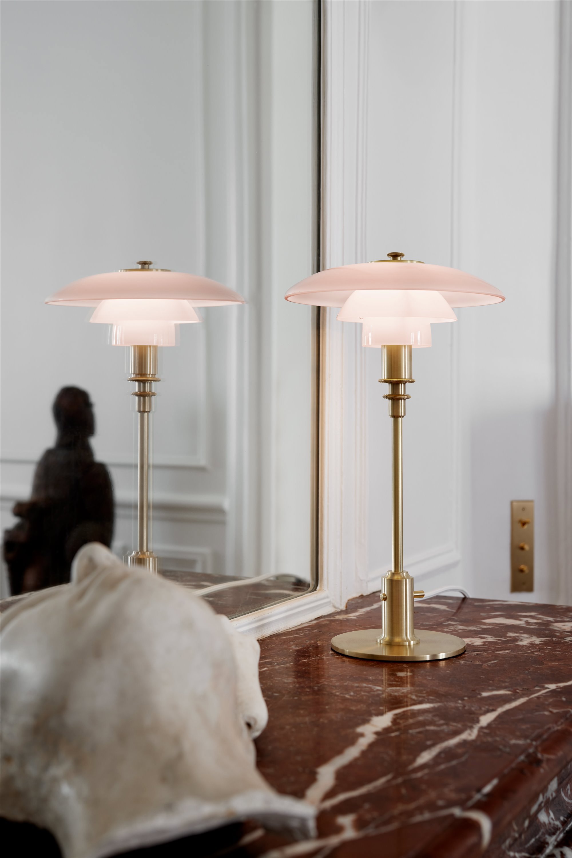 lámpara de mesa rosa con cuerpo de latón vintage sobre una repisa de mármol y un espejo