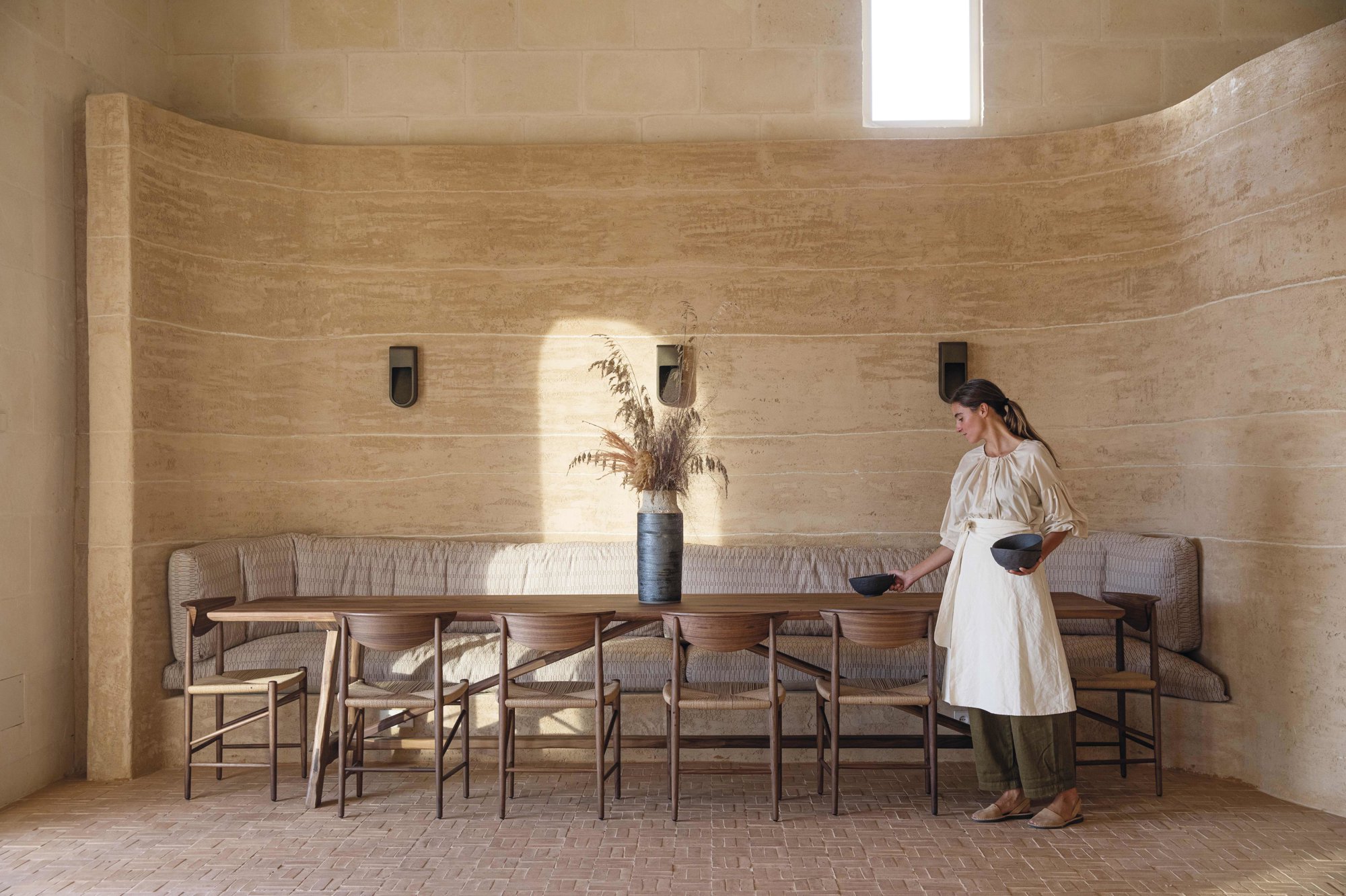 En el comedor de cenas, con suelo de ladrillos artesanales, mesa a medida, de Gavila Carpintería; sillas, de &Tradition; banco de obra integrado en la pared curva con colchonetas con tela de Élitis, y jarrón, de Jose Carvalho.