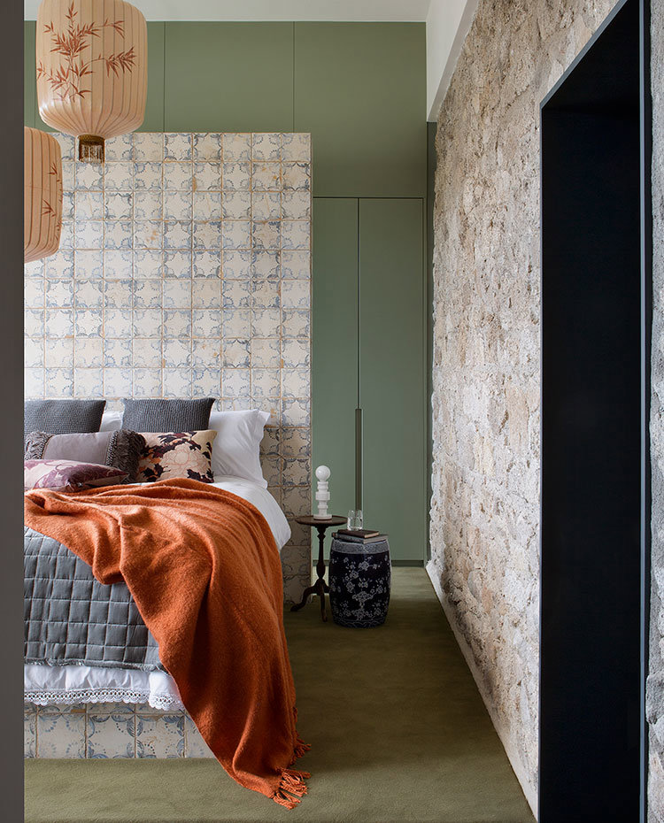 Dormitorio con cabecero de baldosas, pared de piedra vista y frente de armarios en tonos verdes