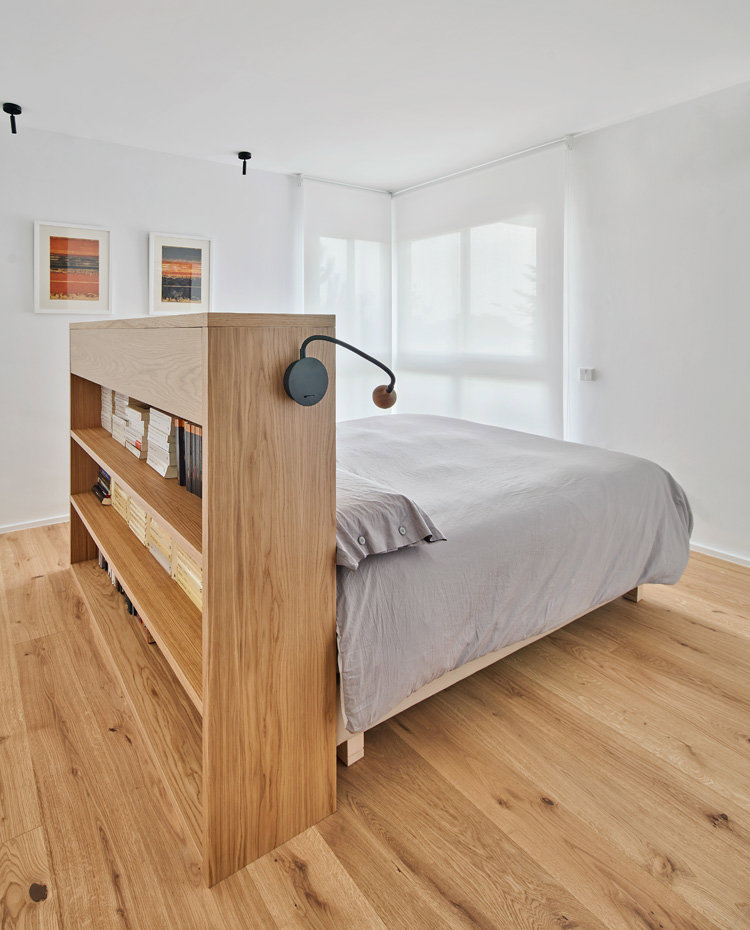 Dormitorio con suelo de madera y cabecero con parte trasera a modo de libreri´a