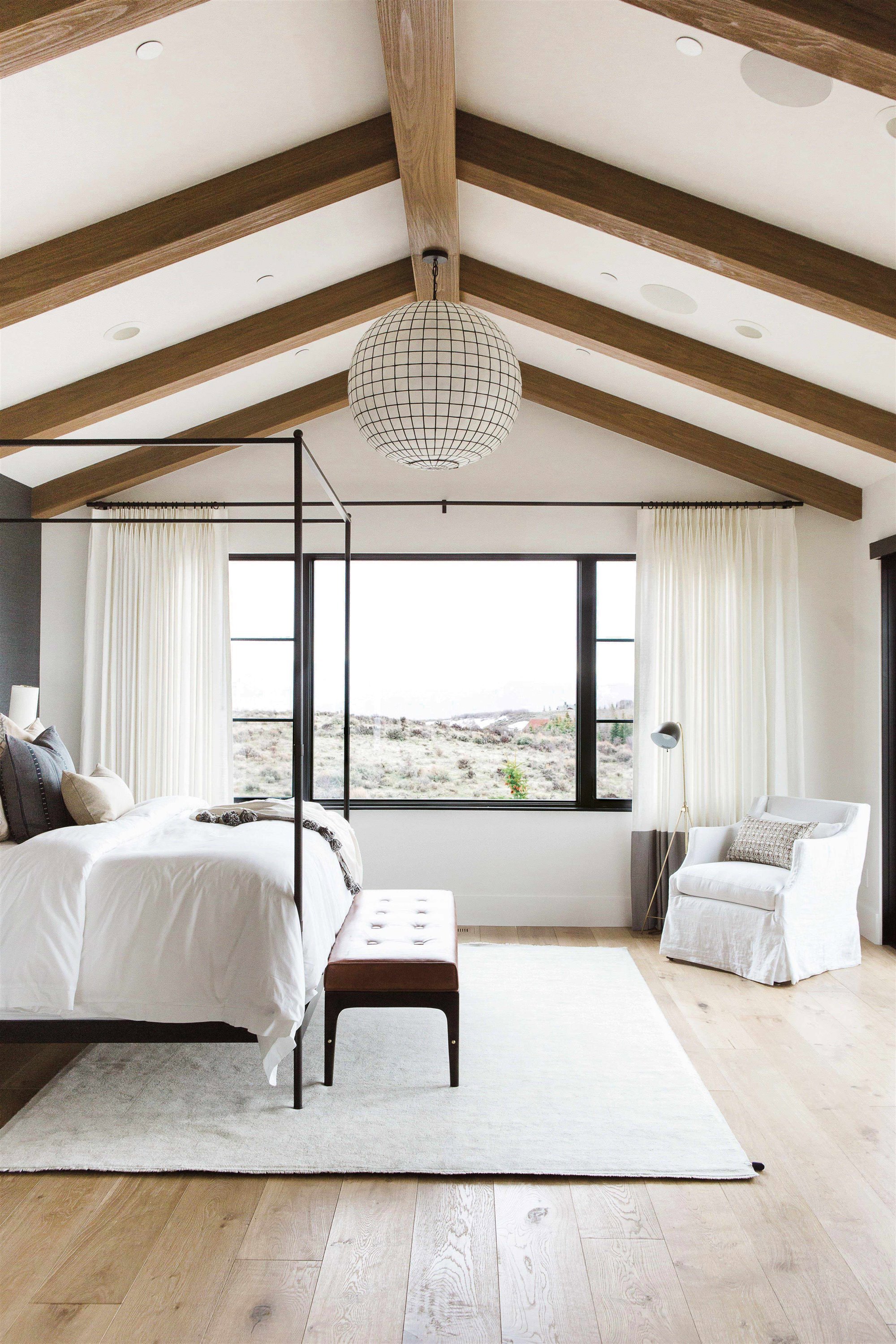 Dormitorio casa de campo minimalista con techo de vigas de madera y cama con dosel negro