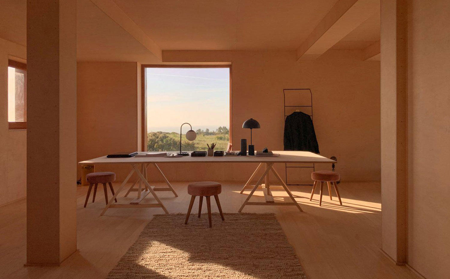 Zona de trabajo con gran mesa de madera y taburetes tapizados en rosa, perchero de pared, alfombras marrones y revestimiento totalmente de madera