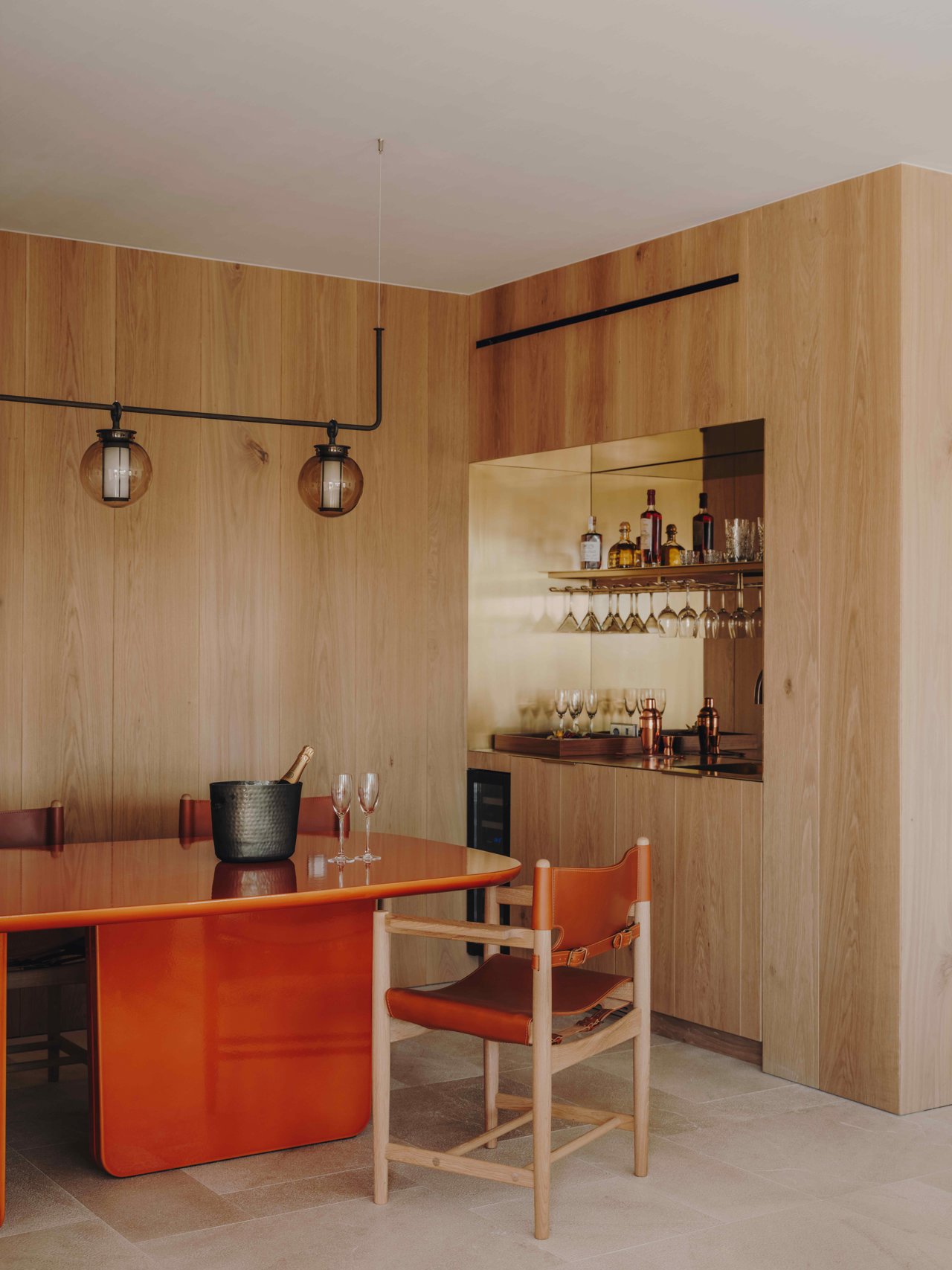 Mesa de Lava esmaltada Pyrolave que contrasta por su color, tamaño y brillo con las paredes de madera de roble o el mueble bar de latón y espejo. Sillas de la colección Spanish Dinning Chair de Fredericia Furniture.