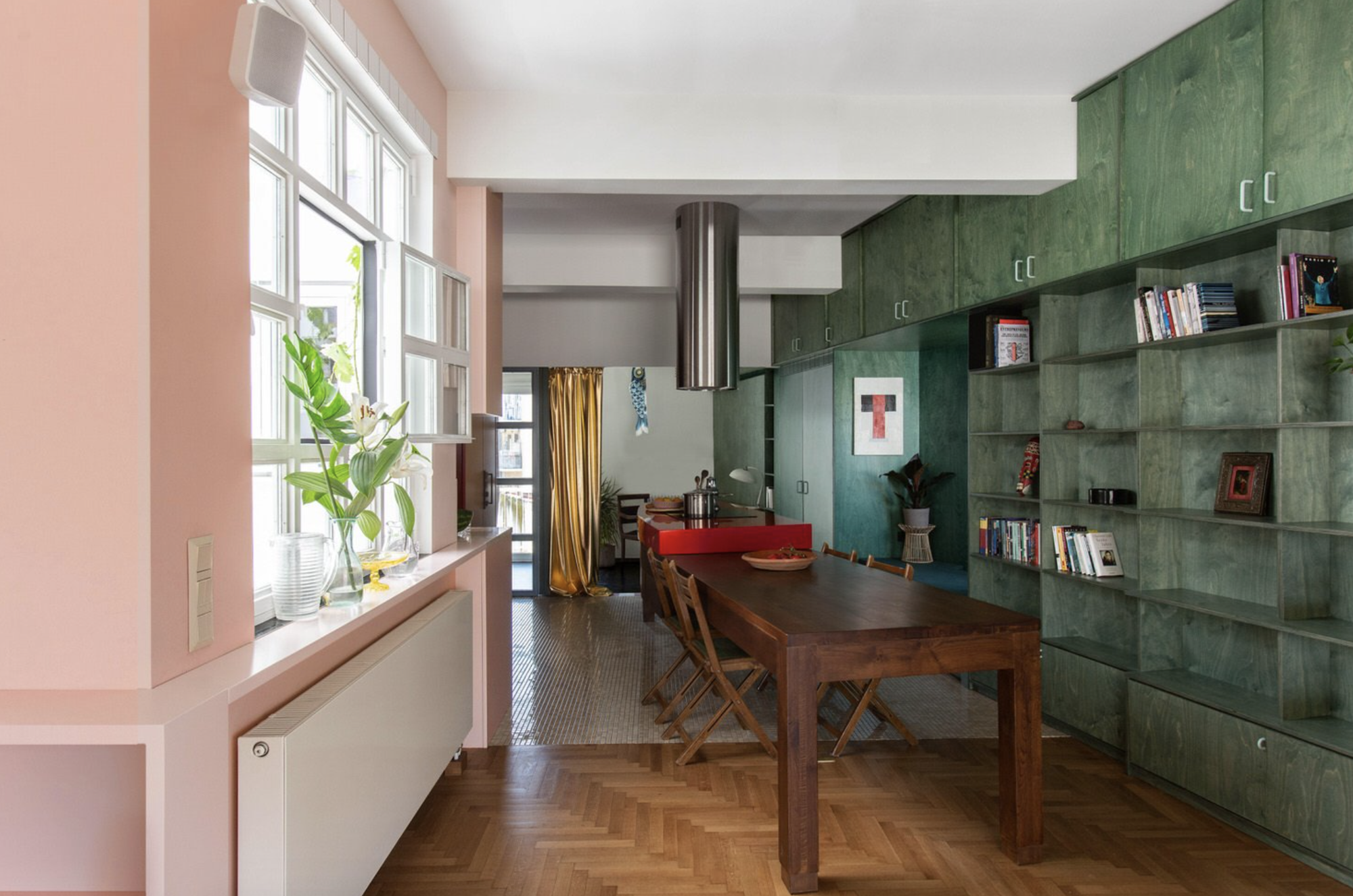 Cocina abierta al comedor con muebles verdes y paredes rosas. 