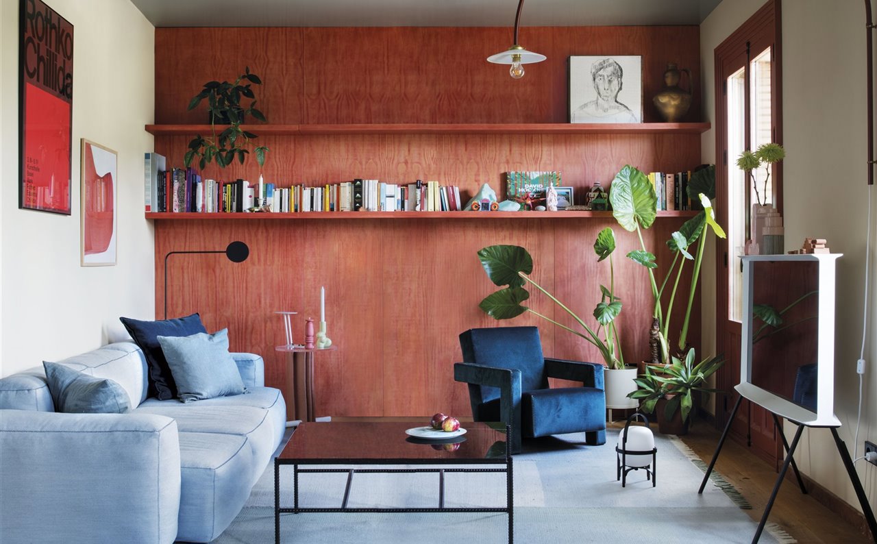 Salón con sofá y butaca en tonos azules, pared en terracota y plantas.