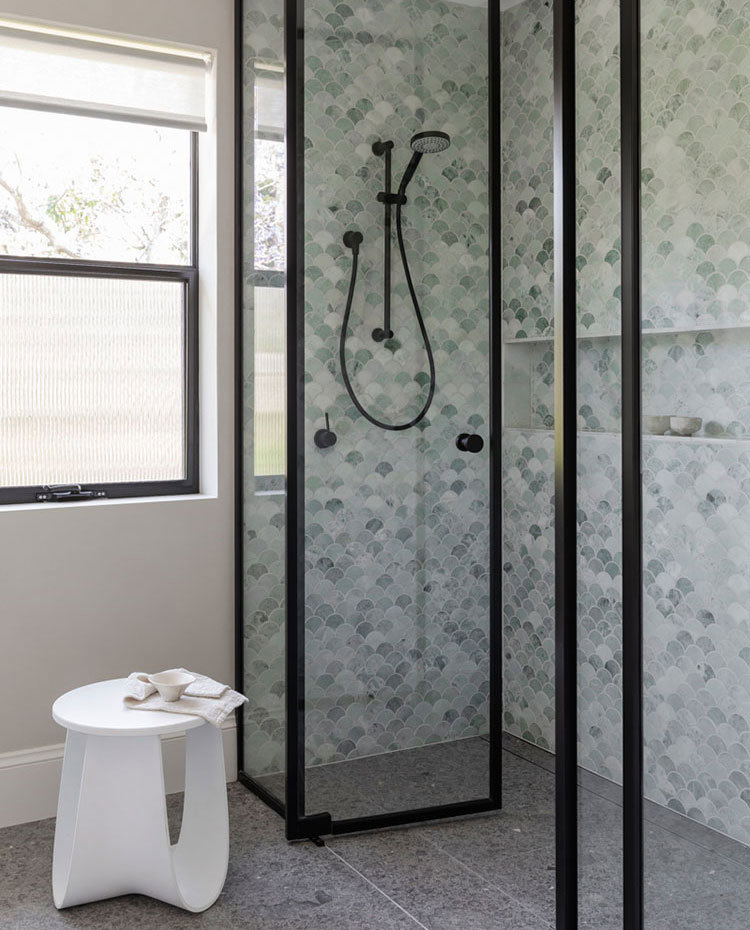 Zona de ducha con cerramiento acristalado a modo de hojas abatibles, perfileri´a en negro, revestimiento de ducha en verde con hornacina de obra, taburete en blanco