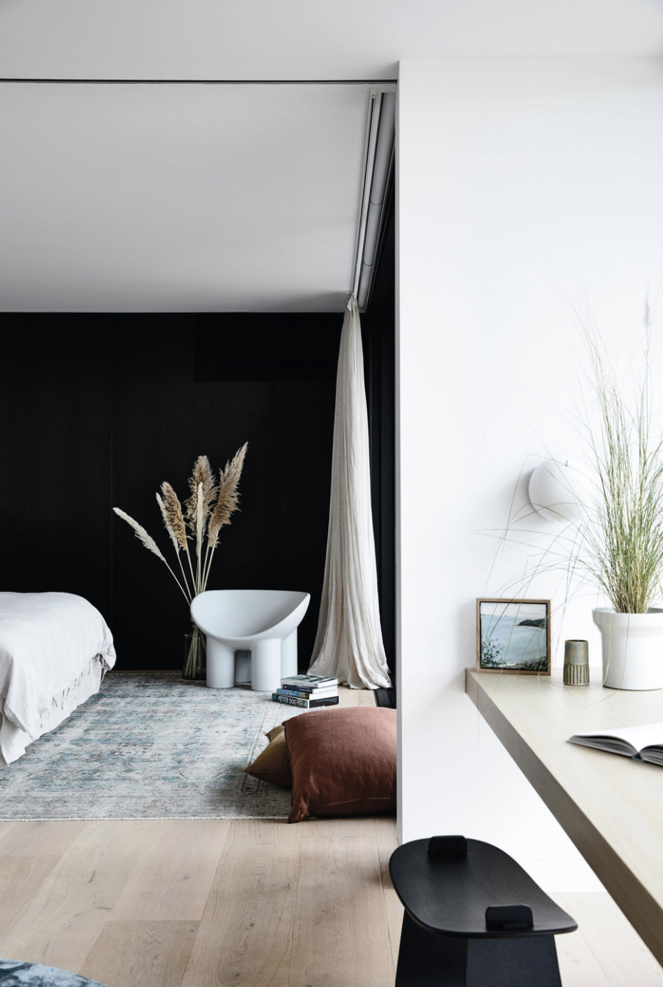 Dormitorio con paredes negras, techo blanco y silla de diseño. 