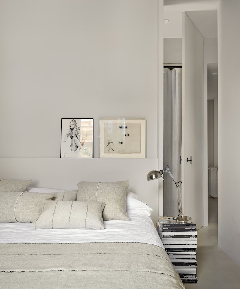 Dormitorio con ropa de- cama y cojines en color blanco de fibras naturales y mesilla de libros.