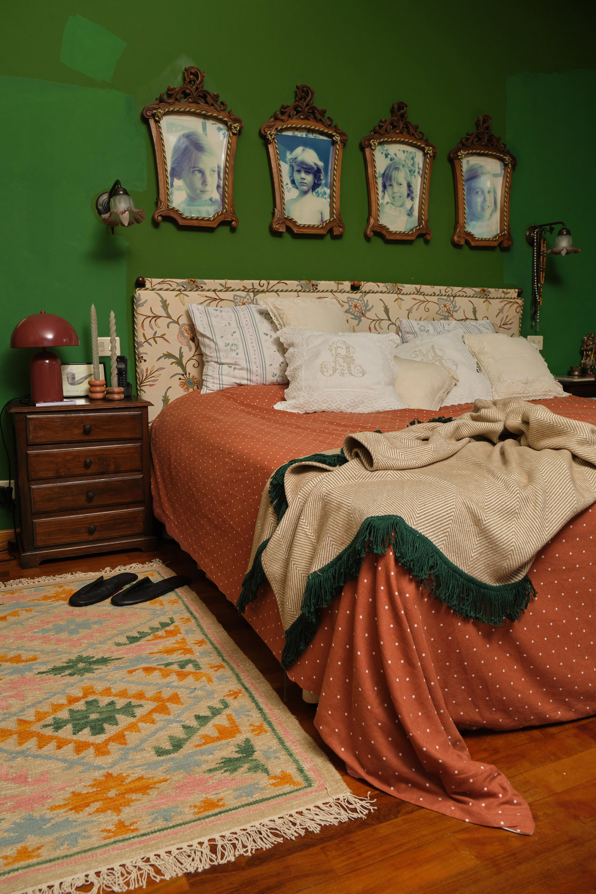 dormitorio con pared verde y retratos de niños en la pared y encima del cabecero