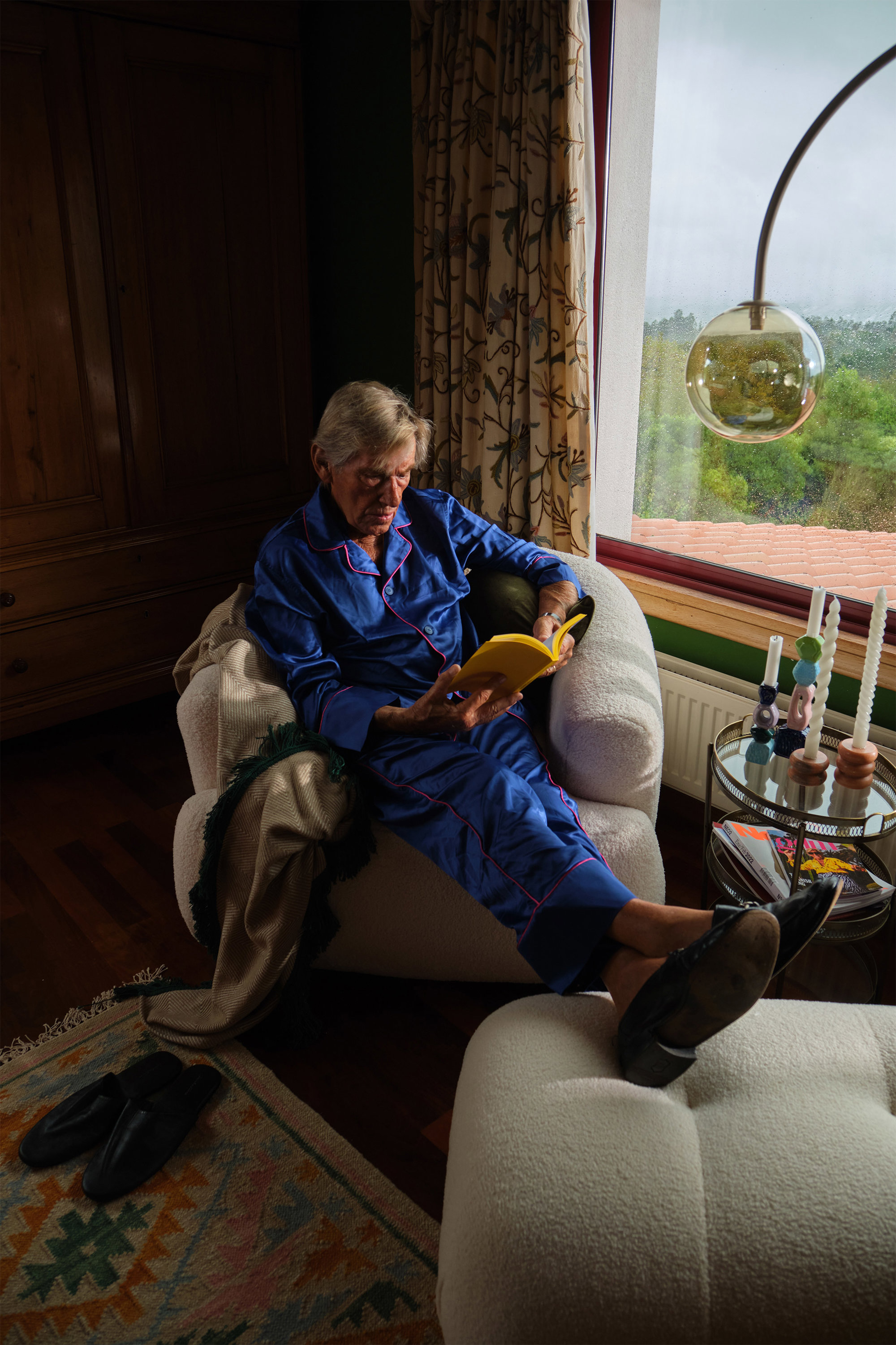 The Spanish King en el dormitorio de su casa de galicia sentado en un sofa de westwing junto a la ventana leyendo un libro