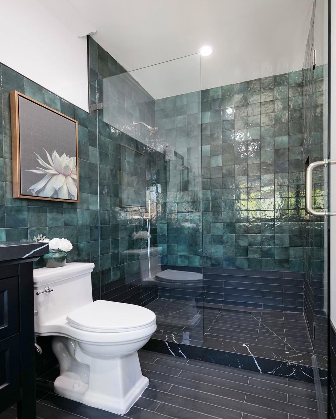 Baño con suelo negro y paredes con azulejos en tonalidades verde