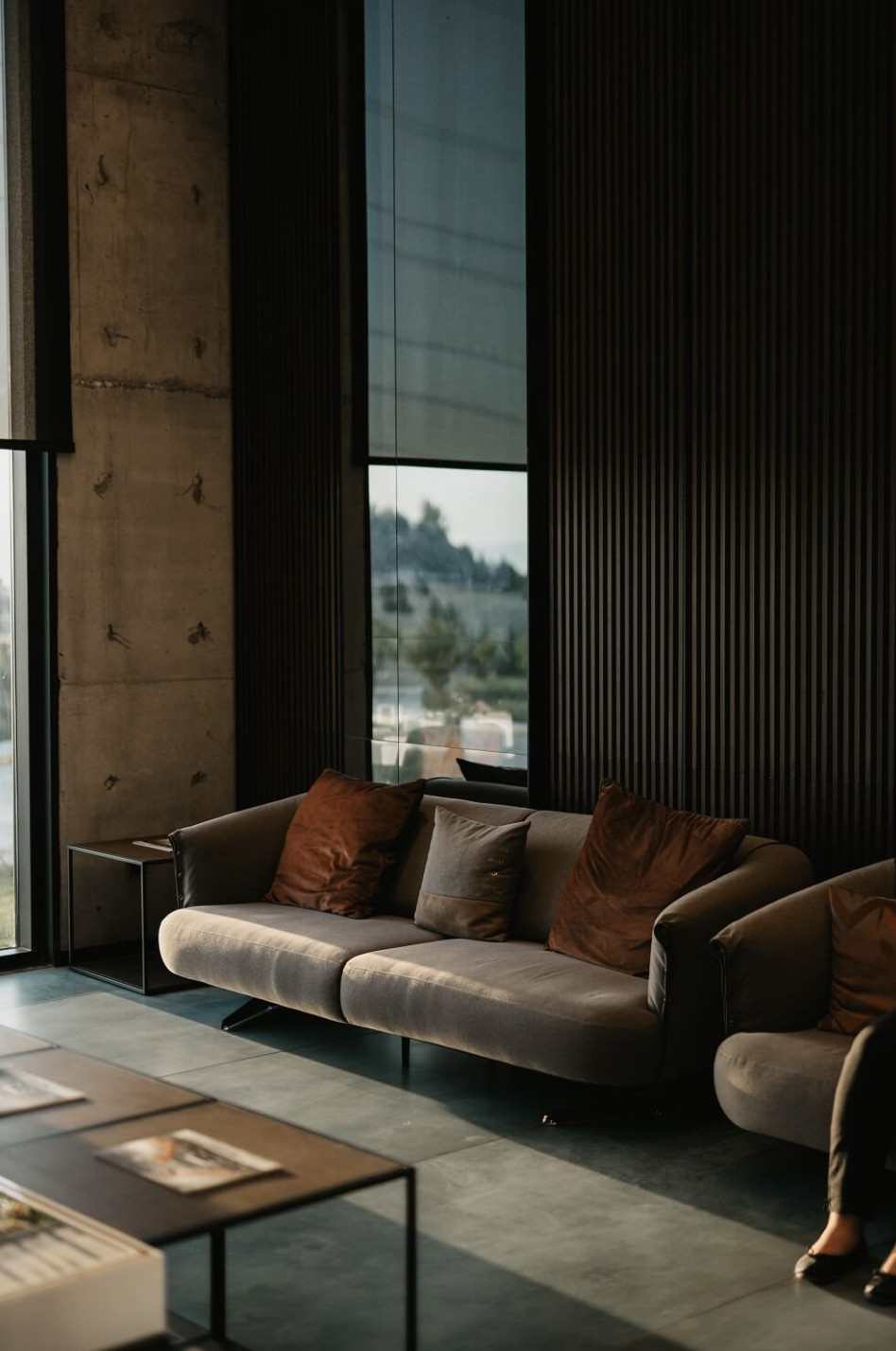 sofa en tonos marrones, pared y suelo de hormigon y ventanas de suelo a techo