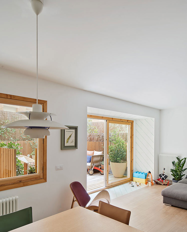Mesa comedor junto a salo´n con sofa´ gris, apertura y ventana hacia exterior de terraza.