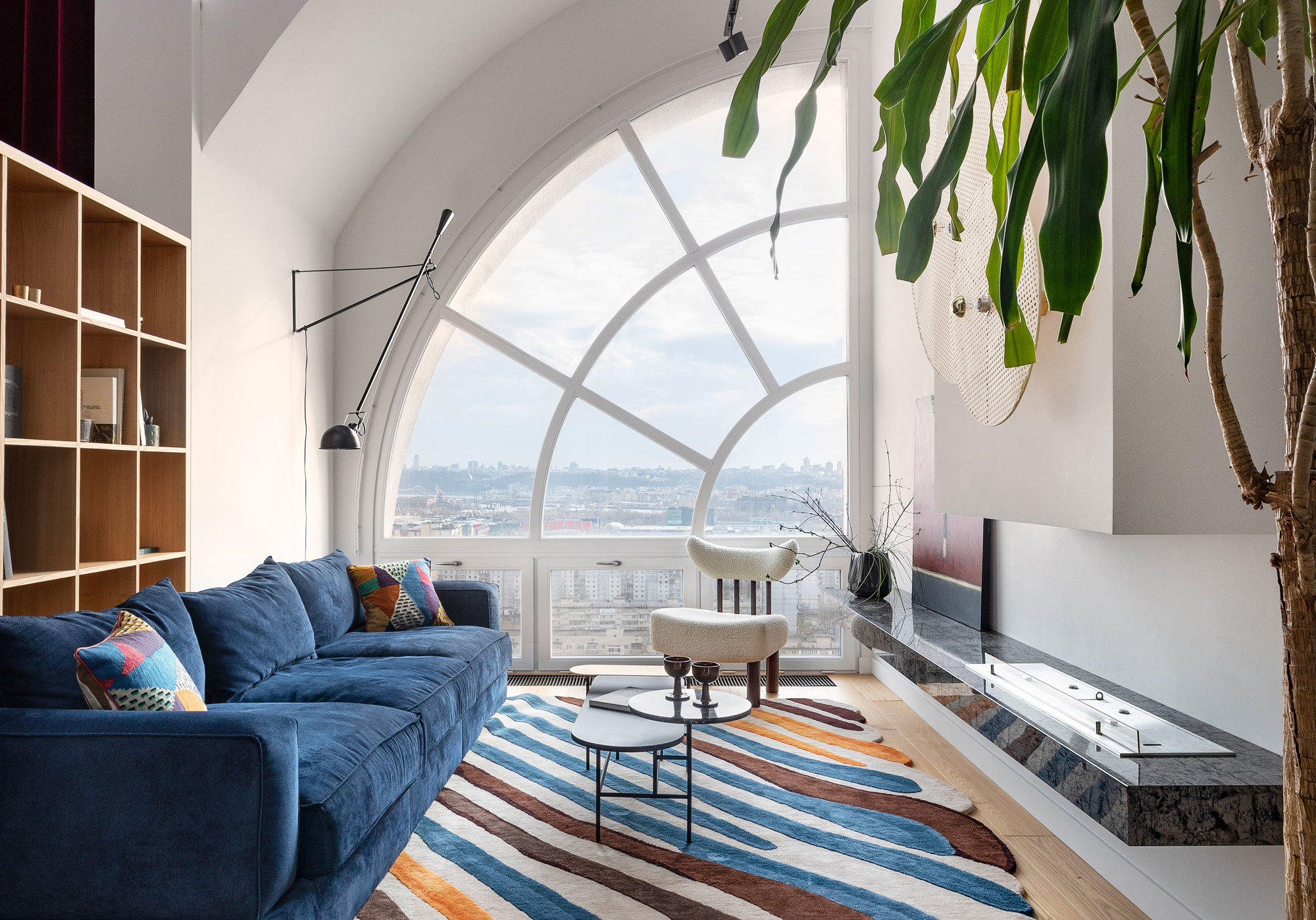 Salón con ventanal grande, sofá azul y alfombra de colores.
