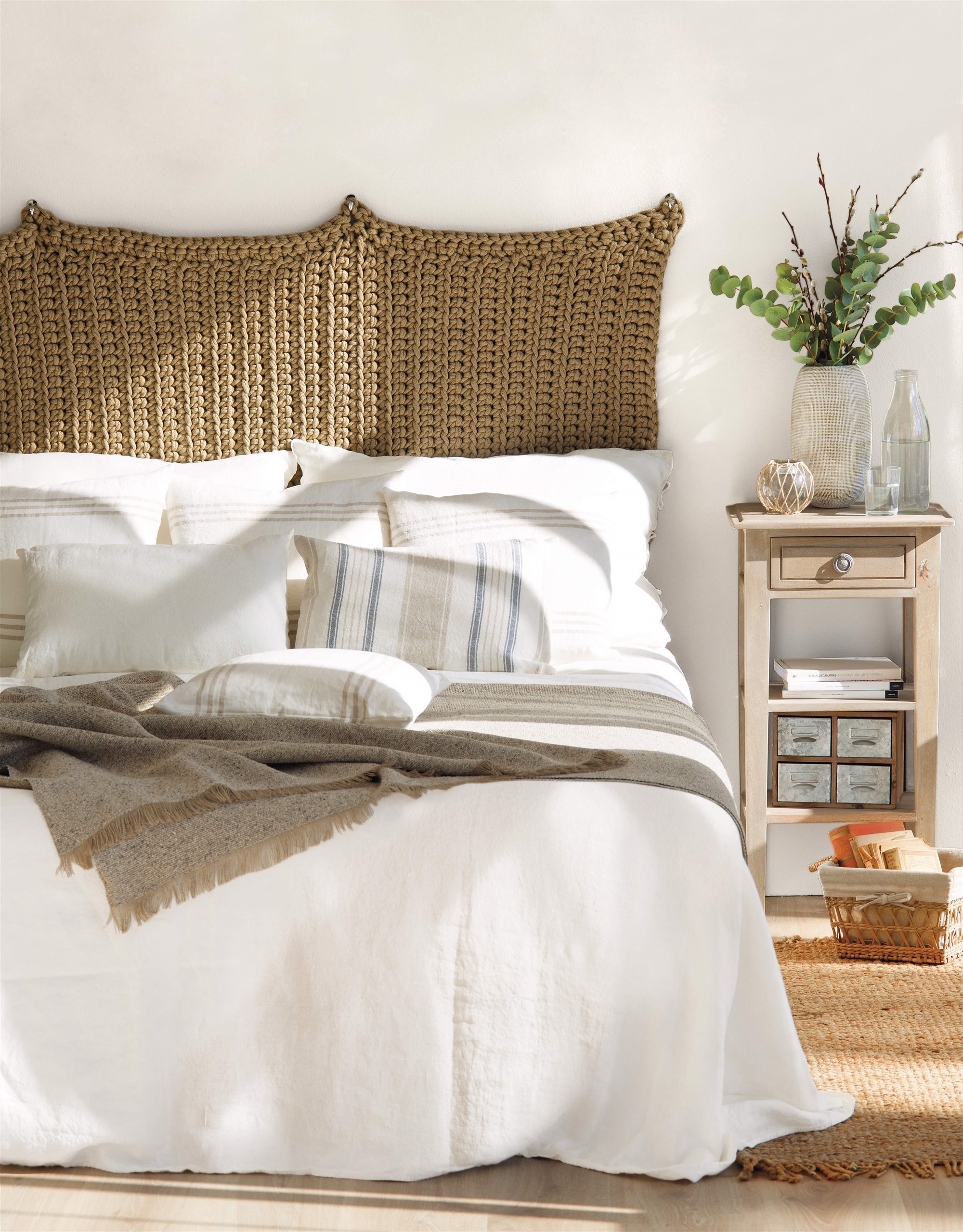Dormitorio blanco con tapiz de macramé a modo de cabecero y alfombra de fibra 