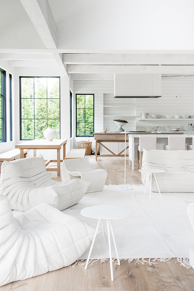 Salo´n con mobiliario en blanco, suelo de madera y comedor y cocina integrados, vistas al exterior de jardi´n.