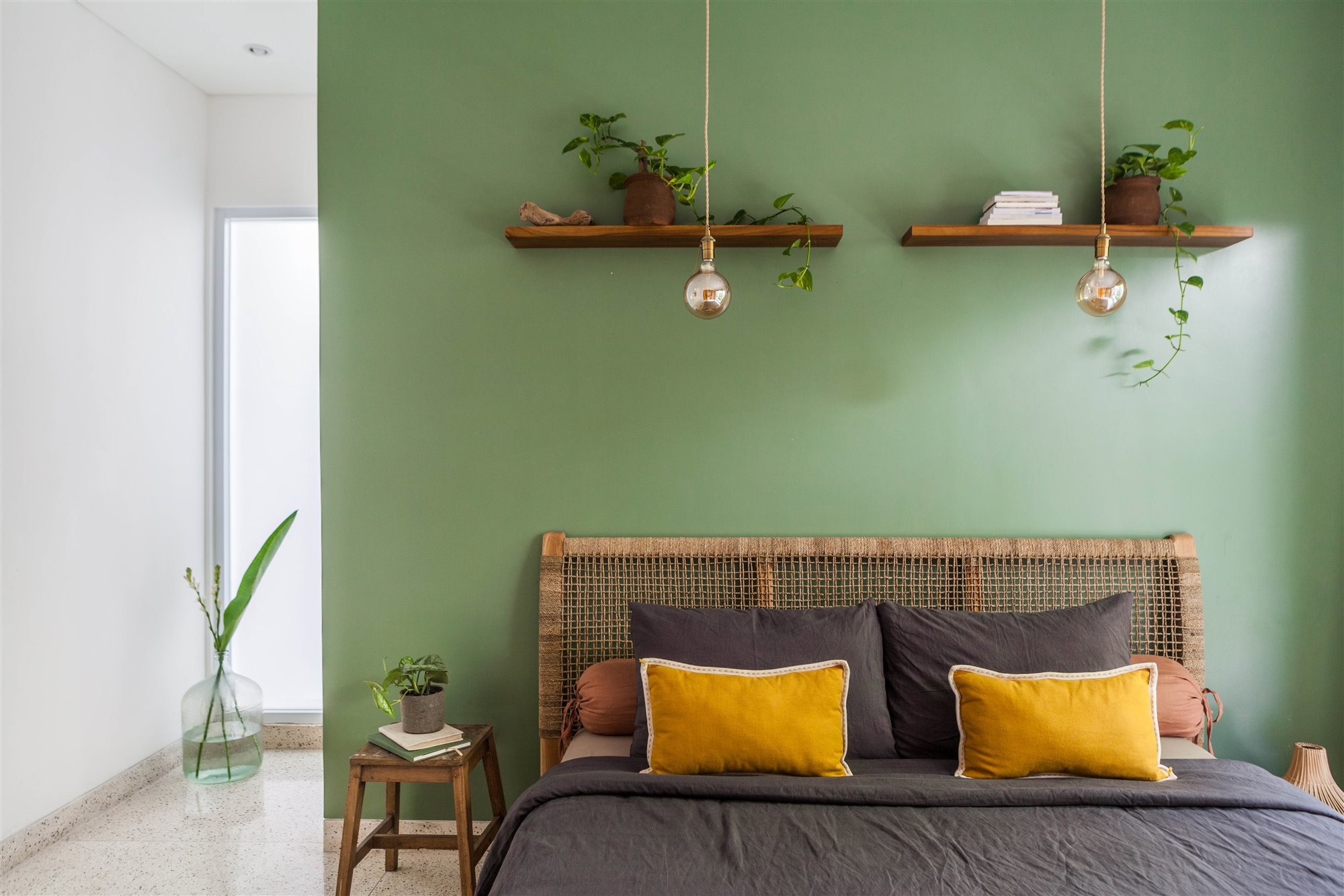Dormitorio con pared verde y estantes en la pared del cabecero.